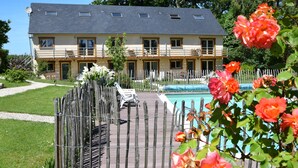 Edifici de dues plantes amb una piscina, envoltat per una tanca de fusta i flors en floració.