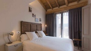 Un dormitorio con cabecera de madera, una mesita de noche con lámpara, una silla y una ventana con cortinas.