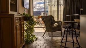 Una habitación acogedora con un armario de madera, una silla de mimbre, una pequeña mesa y vistas a las montañas a través de un ventanal grande.