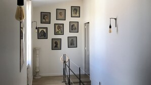 A staircase with a wooden floor, white walls, and black railings. There are framed pictures on the wall and a light fixture above the staircase.