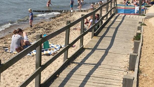 En träpromenad som leder till en sandstrand där folk promenerar och sitter.