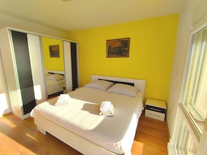 Een lichte, gele slaapkamer met een groot bed, een spiegel en een schilderij aan de muur.