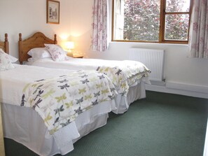 A bedroom with two single beds, a nightstand with a lamp, a window with curtains, and a radiator.