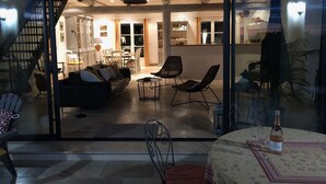 Ein gemütlicher Wohnbereich mit einer Couch, Sesseln und einem Esstisch. Eine linke Wendeltreppe führt auf eine höhere Ebene.