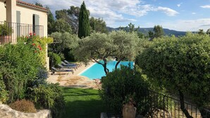 Ein Poolbereich mit Liegestühlen, einem großen Baum und Blick auf ferne Hügel.