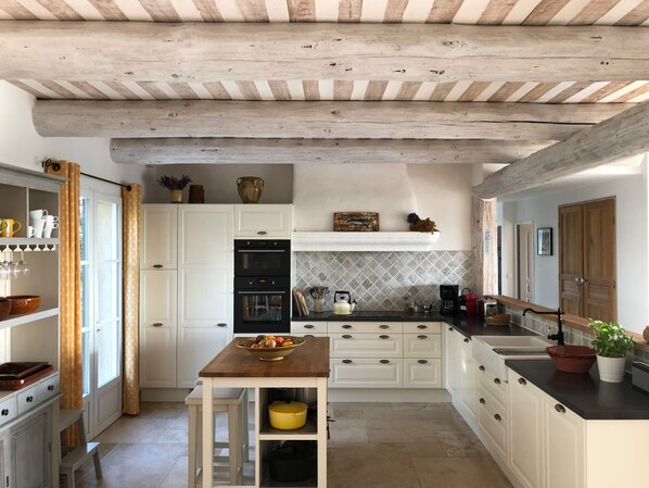 Una cucina con mobili bianchi, un tavolo in legno e un rivestimento a piastrelle.
