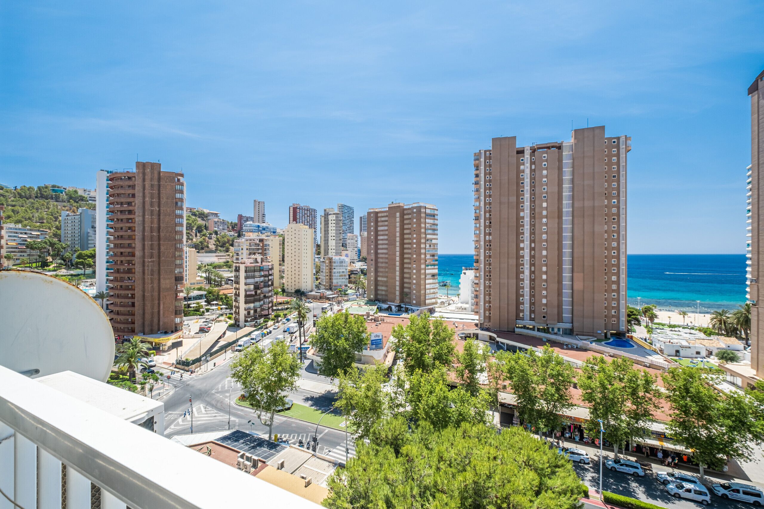 Paisagem costeira urbana com edifícios altos, céu azul claro e vista para o mar.