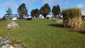 A grassy area with several white buildings, large rocks, and trees. -  Chalet Cwtch, a cosy 5 bed holiday cottage in Roch, Pembrokeshire (Roch)