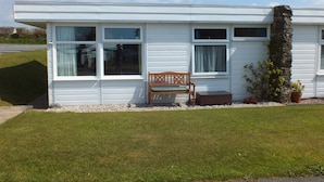 A single-story building with large windows, a bench, and a potted plant. -  Chalet Cwtch, a cosy 5 bed holiday cottage in Roch, Pembrokeshire (Roch)