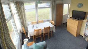 A compact room with a dining table, chairs, a sofa, a television, and a bookshelf. -  Chalet Cwtch, a cosy 5 bed holiday cottage in Roch, Pembrokeshire (Roch)