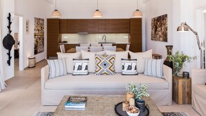 A modern living room with a sofa, decorative pillows, a coffee table with books and a plant, and pendant lighting. - THETIS, south coast with amazing views and infinity pool! (Chania)