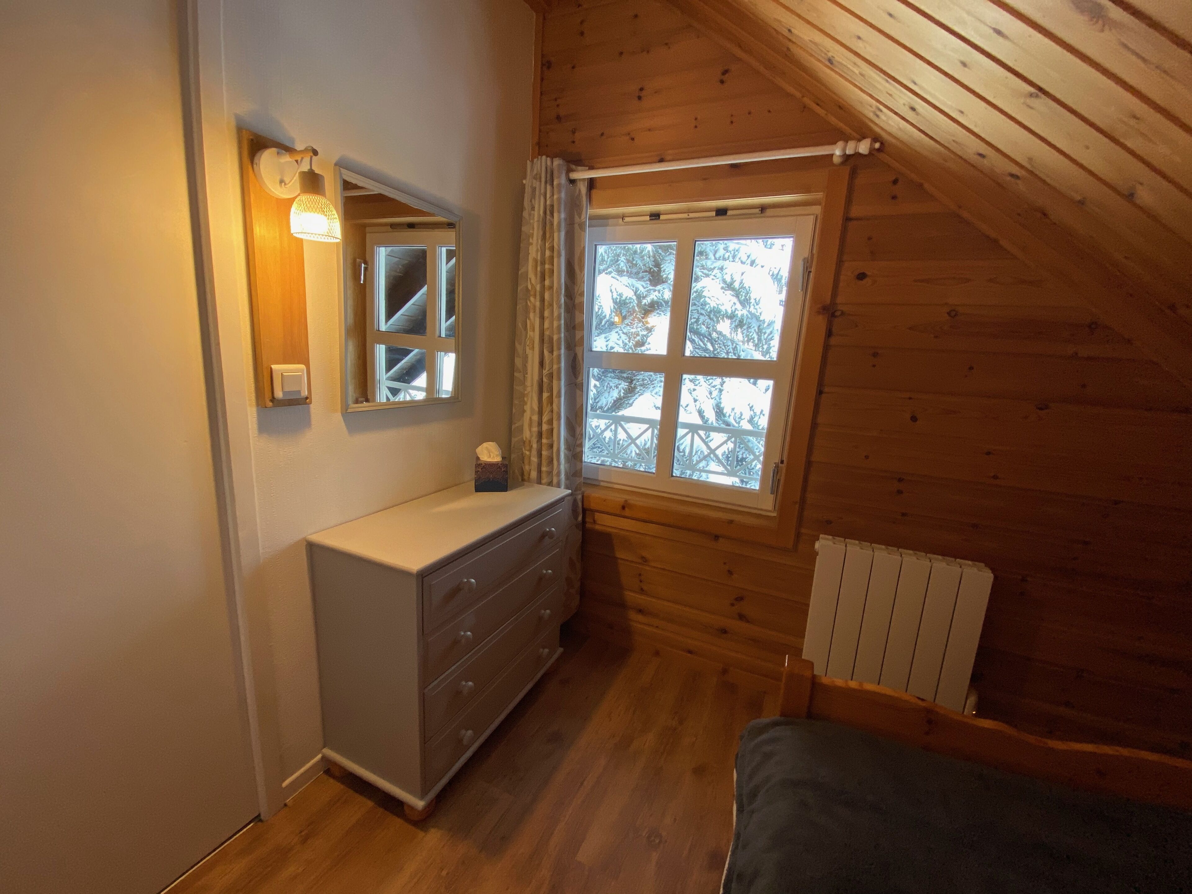 Ein Schlafzimmer mit Holzboden, einem Schminktisch, einem Fenster mit Blick auf Bäume und einer Heizung.