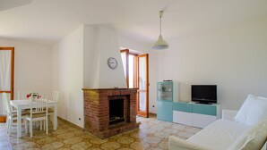 A living room with a brick fireplace, a dining table with chairs, a sofa, a television on a cabinet, and a clock on the wall. - Holiday home on the amazing Cilento Coast in the south of Italy (Case del Conte)