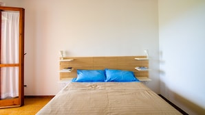 A bedroom with a wooden headboard, a bed with a beige bedspread, two blue pillows, and a nightstand with a lamp and books. - Holiday home on the amazing Cilento Coast in the south of Italy (Case del Conte)