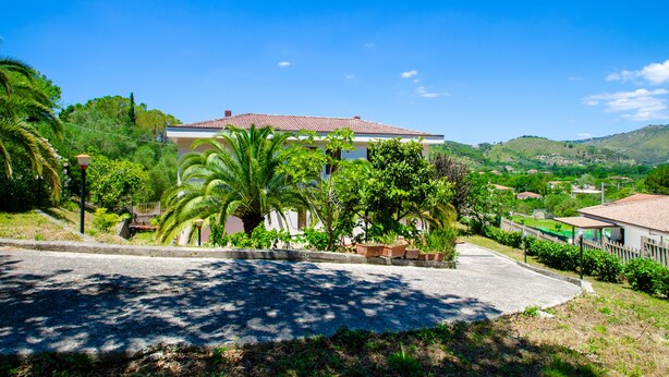 A house with a red-tiled roof, surrounded by lush greenery and palm trees. - Holiday home on the amazing Cilento Coast in the south of Italy (Case del Conte)