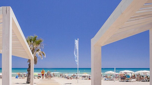 Une plage agrémentée de pergolas blanches, de palmiers et de parasols.