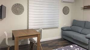 Un salon avec une table en bois, deux chaises blanches, un canapé gris et des assiettes décoratives accrochées au mur.