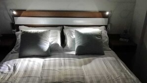 Un lit bien fait, avec une literie à rayures et deux oreillers, une tête de lit en bois et une lampe de chevet.