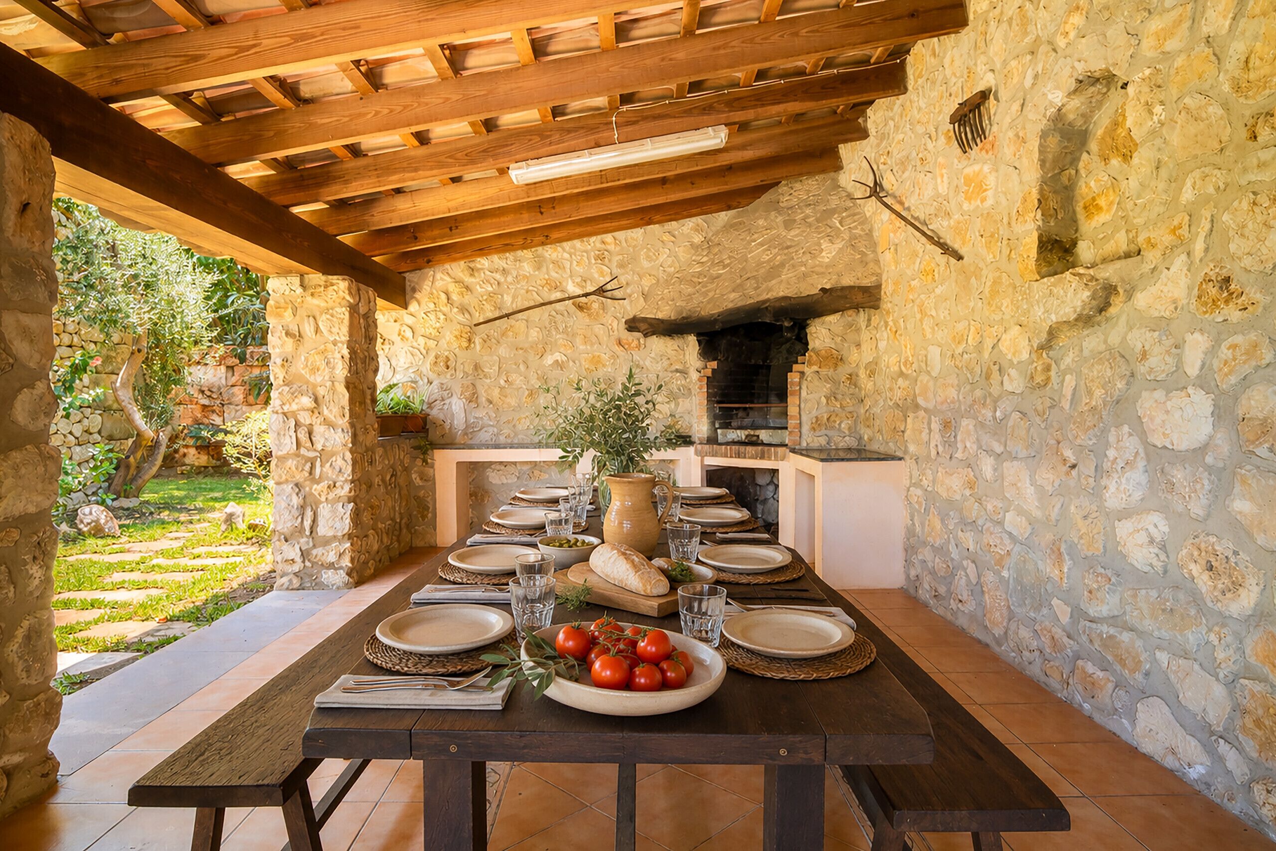 An outdoor dining area with a stone wall, wooden ceiling, and a brick oven.
