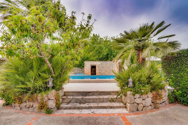 A stone staircase leading to a small building with a blue-tiled entrance, surrounded by lush greenery and palm trees.