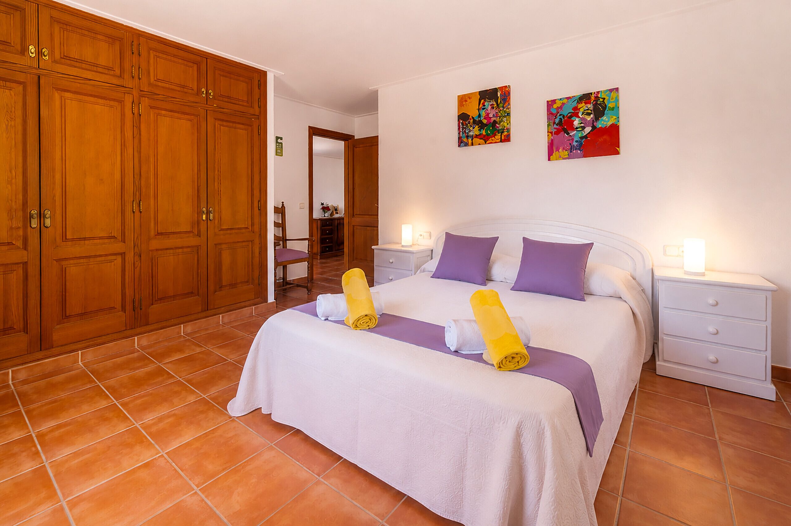 Une chambre d’hôtel avec un grand lit, deux tables de chevet, une armoire en bois et deux tableaux au mur.