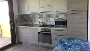A modern kitchen with light wood cabinets, a stainless steel sink, a gas stove, a microwave, and a patterned tablecloth. - Two-room apartment in Palau, 20 minutes from the Costa Smeralda in Sardinia (PALAU (OT))