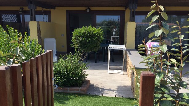 A yellow building with a covered patio area, a small table, and a white chair. - Two-room apartment in Palau, 20 minutes from the Costa Smeralda in Sardinia (PALAU (OT))