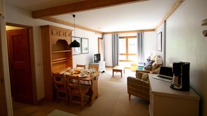 A cozy living room with a dining area, wooden furniture, a television, and a laptop on a desk.