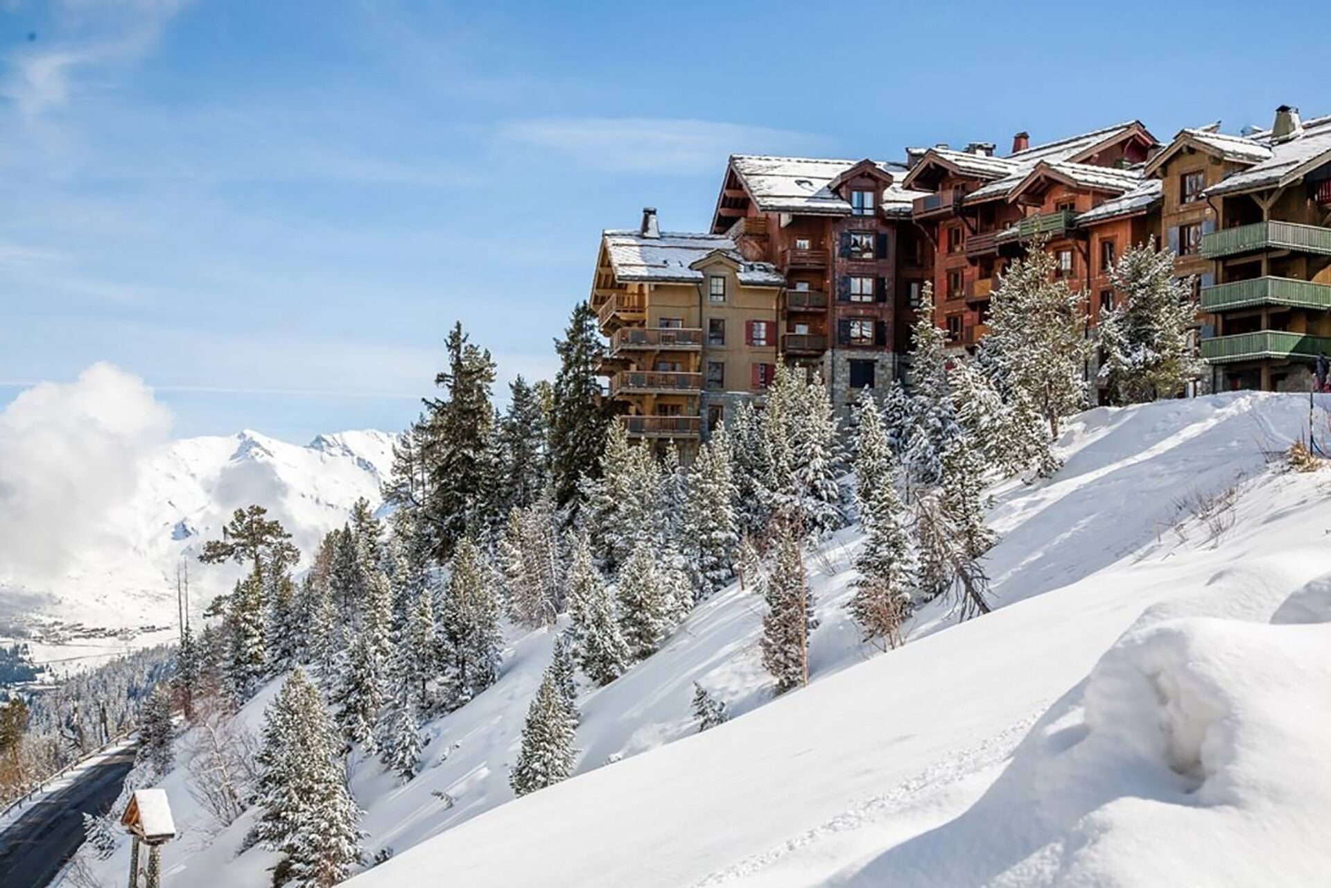 Una montagna innevata con un complesso turistico sciistico dotato di numerosi balconi e un cielo sereno.