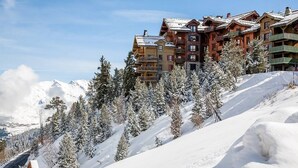 A snow-covered mountain with a ski resort building featuring multiple balconies and a clear sky.
