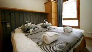 A neatly made bed with striped bedding and a rolled towel, a wooden headboard, and a window with curtains.