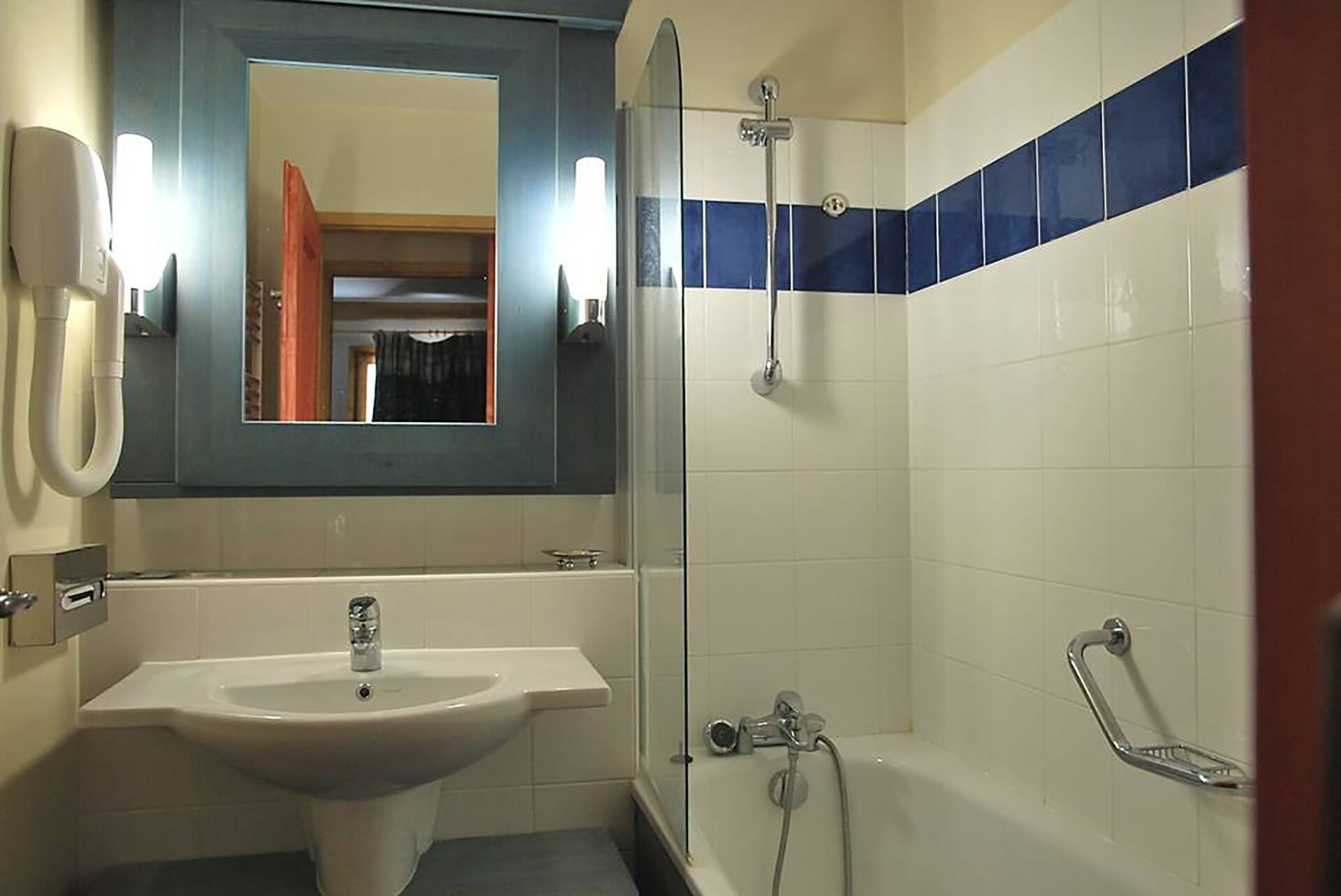 A bathroom with a sink, mirror, shower, and a tiled wall.