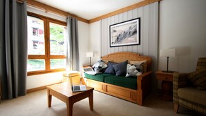 A cozy living room with a wooden sofa, a green throw blanket, and a laptop on a wooden coffee table.