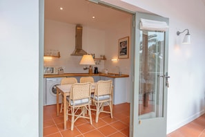 A kitchen with a dining table, chairs, a washing machine, and a glass door leading outside.