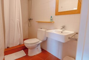 A bathroom with a toilet, sink, shower, and a shelf with a bottle. - ApartmentsTamariu#5 🌊 Cozy Retreat with Terrace (Tamariu)
