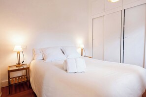 A neatly made bed with white linens and towels, two bedside lamps, a wooden nightstand, and a wardrobe with a sliding door. - ApartmentsTamariu#5 🌊 Cozy Retreat with Terrace (Tamariu)
