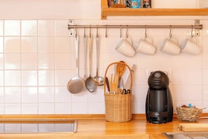 Une cuisine avec des ustensiles suspendus, une machine à café et un panier contenant des outils de cuisine.