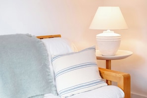 A chair with a grey blanket, a white pillow with blue stripes, and a white lamp on a small table.