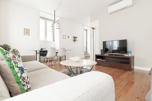 Una sala moderna con un sofá, una mesa redonda de centro, un televisor y un comedor con sillas y una mesa.