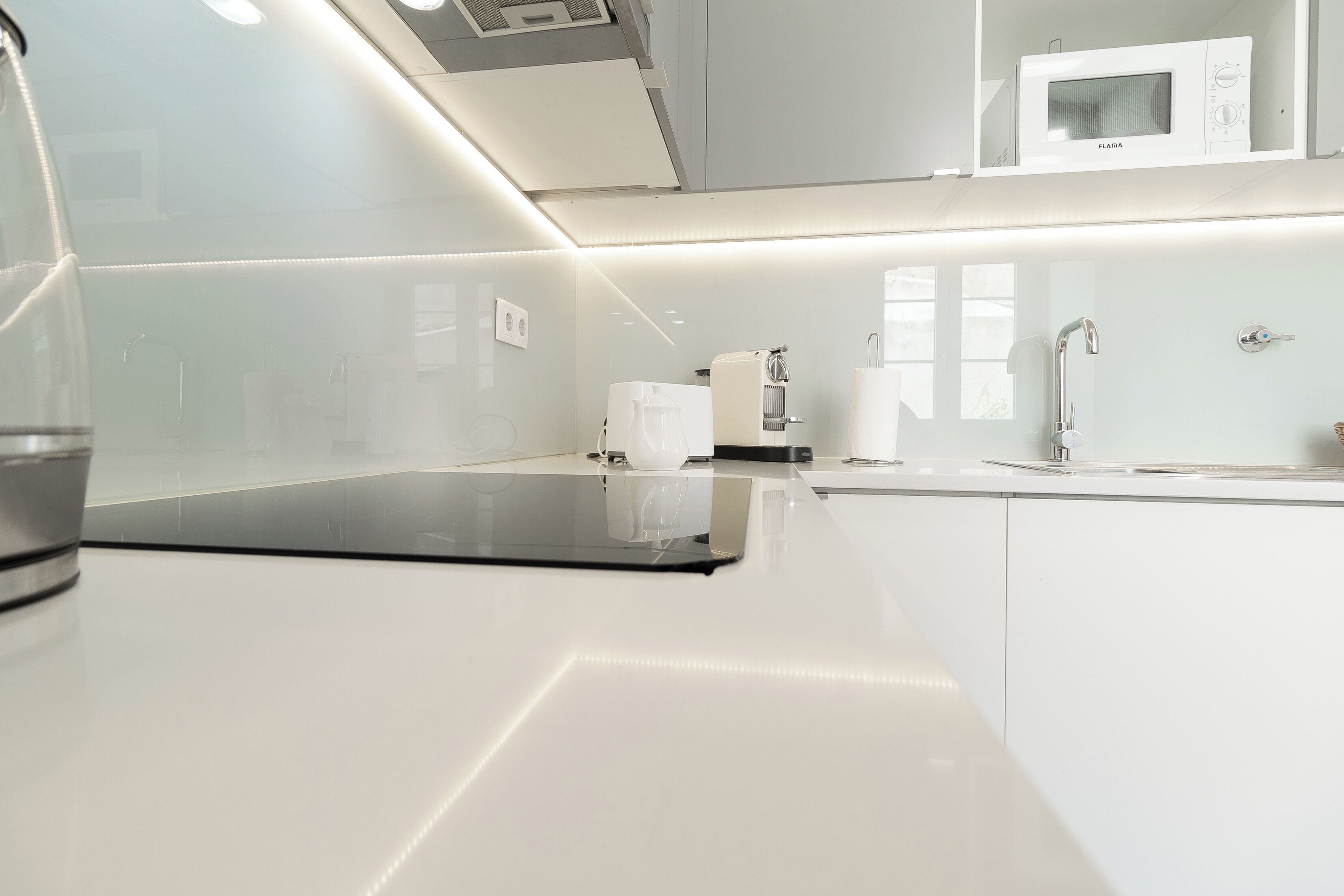 Een moderne keuken met witte kastjes, een ingebouwde magnetron en een koffieapparaat.