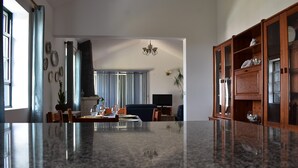 Ein geräumiges Wohnzimmer mit großem Marmorboden, einem Fernseher und einem Essbereich mit Stühlen und Tisch.