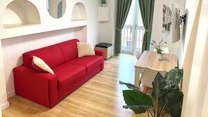 A modern living room with a red sofa, a wooden dining table, and a large green plant. - SuiteCorso Vibo Valentia (Vibo Valentia)