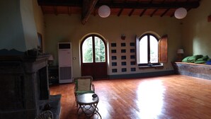 Una habitación con chimenea, dos ventanas arqueadas, una mesa y una silla.