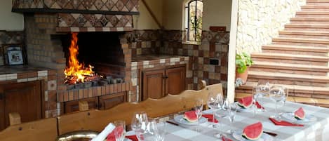 An outdoor dining area with a brick fireplace, a checkered tablecloth, and a stone staircase.