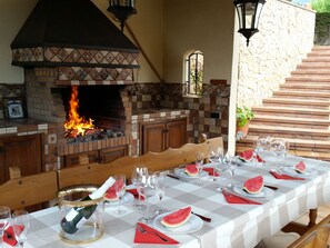 Un espace extérieur aménagé pour les repas, avec une cheminée en briques, une nappe à carreaux et un escalier en pierre.