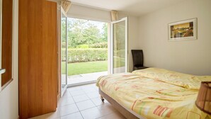 Un dormitorio con una cama, un armario de madera, un ventanal corredero a un jardín y un cuadro enmarcado en la pared.