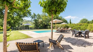Zona junto a la piscina con sillas de descanso, una mesa y sombrillas.