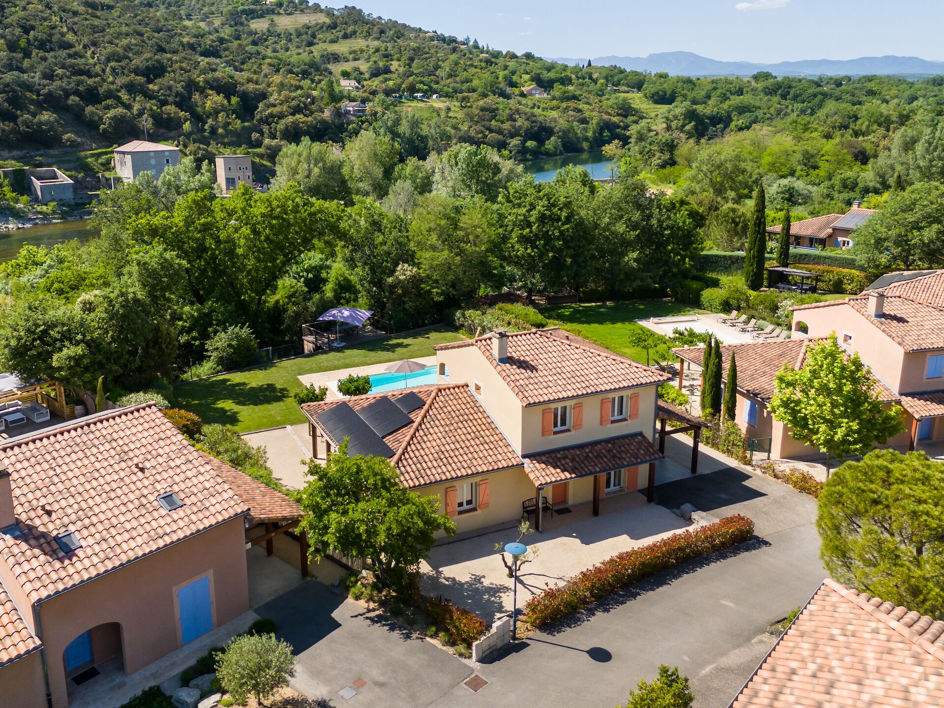 A residential area with houses, a swimming pool, and a view of a lake surrounded by greenery.