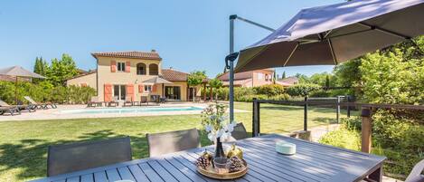 Un patio con una mesa lista para comer, una piscina y una casa al fondo.