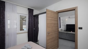 Ein Schlafzimmer mit einem Bett, einer Holztür, einem Fenster mit Vorhängen und einem Wohnbereich mit einer Couch und einem Fernseher.